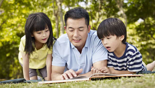 two children reading a book with their father