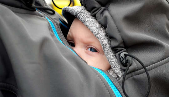 a baby sheltered inside his mother's jacket on her breast