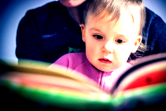 a child sitting on his mother's lap and reading from a book