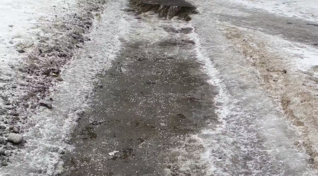 A snowy sidewalk covered in tiny chunks of salt.