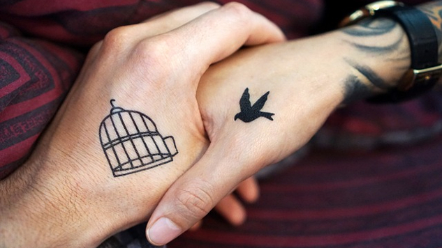 two clapsed hands... one with an open bird cage tattoo, one with a bird in flight