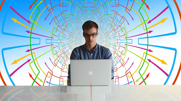 man sitting at a computer with a complicated drawing of charts and graphs behind him