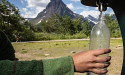 a person refilling a drinking water bottle from a outside spigot